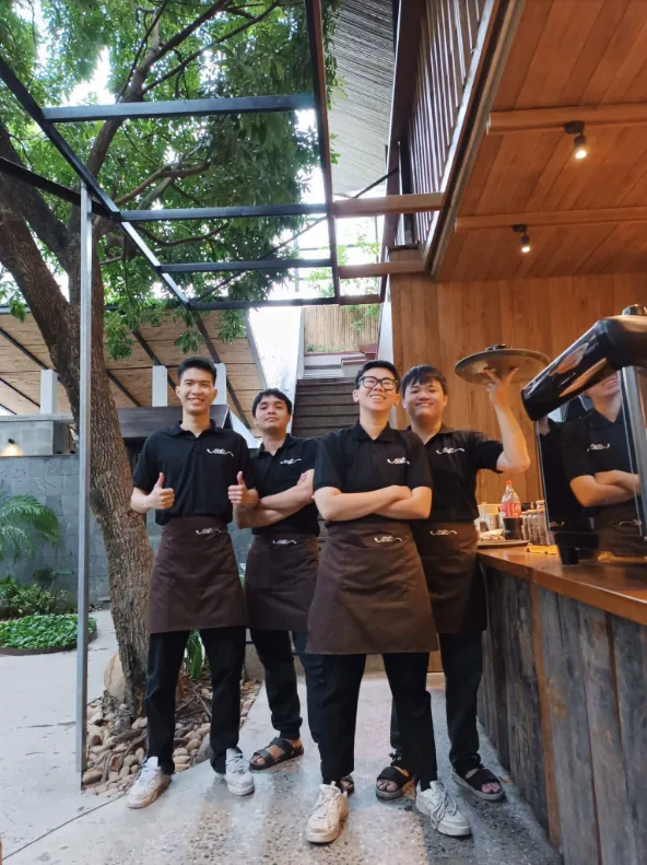 Nhân viên NiA Coffee mặc áo polo đen và tạp dề nâu